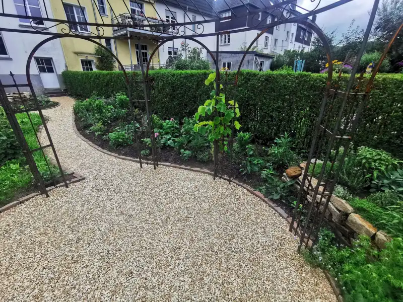 Kiesweg zwischen Beeten unter Rankbögen