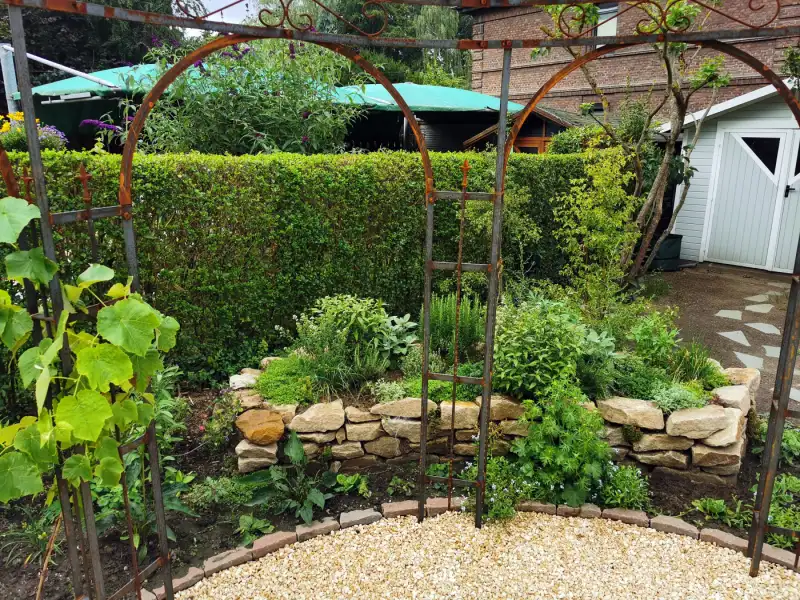 Trockenmauer am Gartenhaus mit Rankbögen
